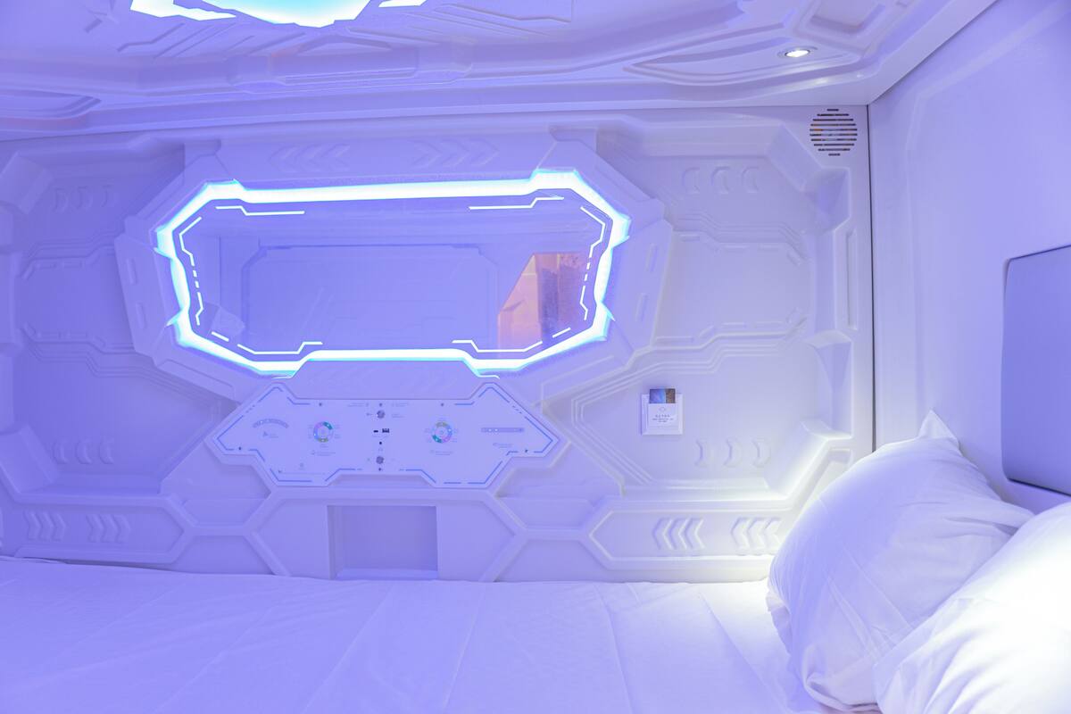 A room with a bed, a control panel, and a large illuminated window.