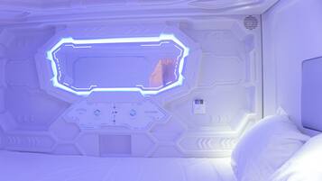 A room with a bed, a control panel, and a large illuminated window.