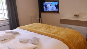 Habitación de hotel con cama, televisor en la pared, cómoda y ventana con cortinas.