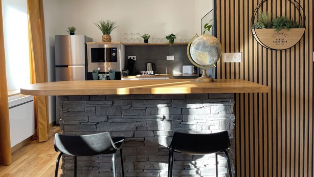 Una cocina moderna con encimera de madera, dos taburetes de bar, un adorno con forma de globo terráqueo y una planta en maceta en la pared.