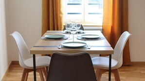 Un comedor con una mesa dispuesta para cuatro personas, sillas blancas y una ventana con cortinas.