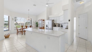 A spacious kitchen with a large island, white cabinetry, and a dining area with wooden chairs.