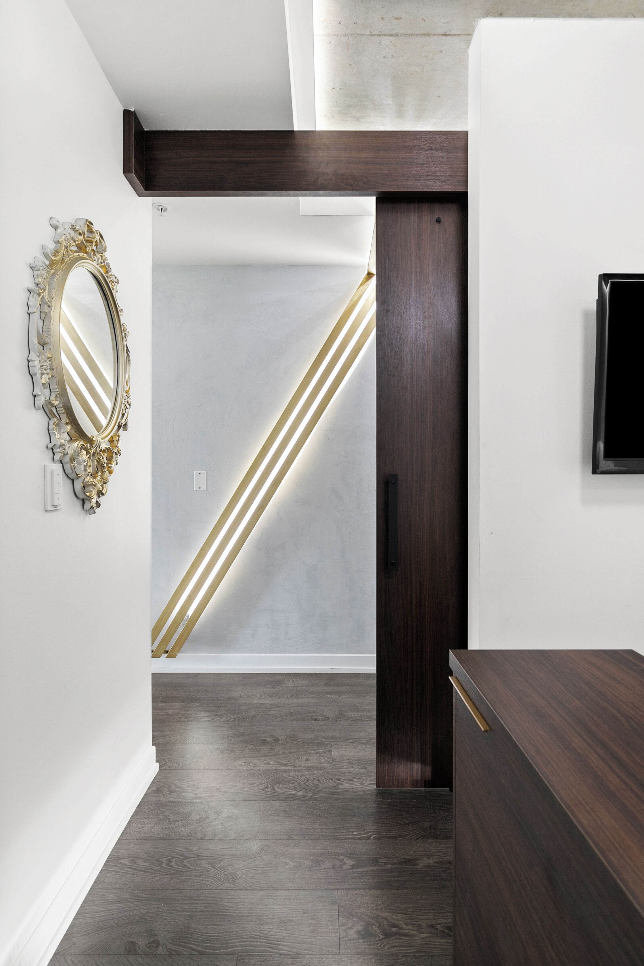 A modern interior with a wooden floor, a dark wooden door, a white wall, and a decorative mirror.