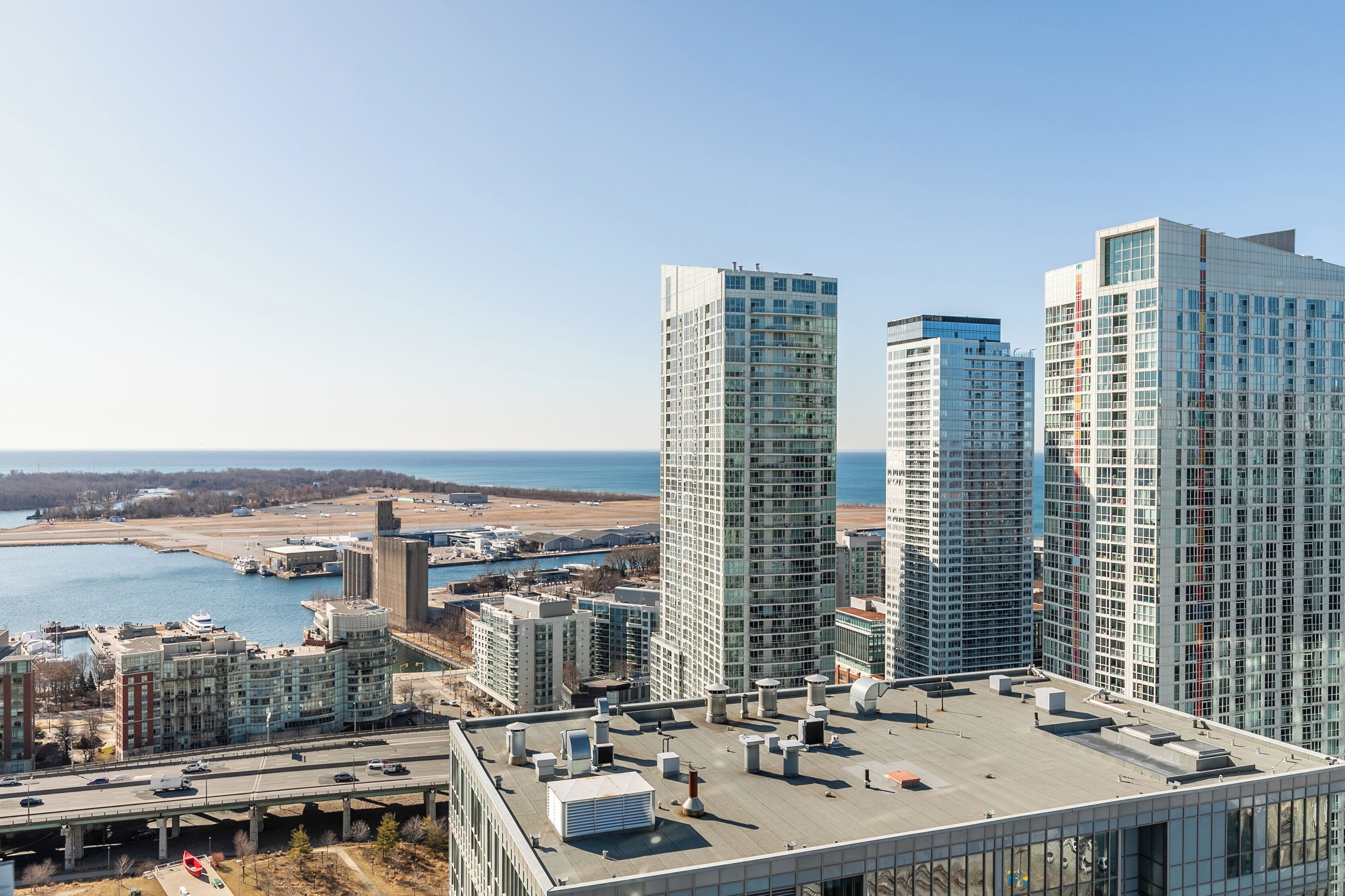 A high-rise building with a modern glass facade, located near a waterfront with a marina and a bridge.