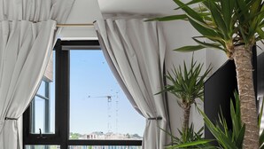A bedroom with a large bed, a view of a cityscape, and two potted plants. - Ohio Global Stay (Toronto)