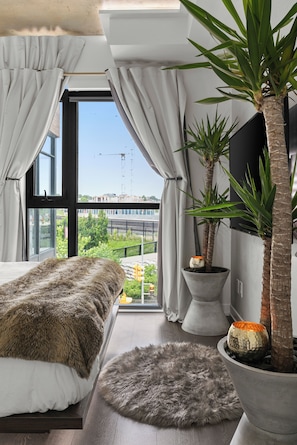 Quarto com cama grande, vista para a cidade e duas plantas em vasos.