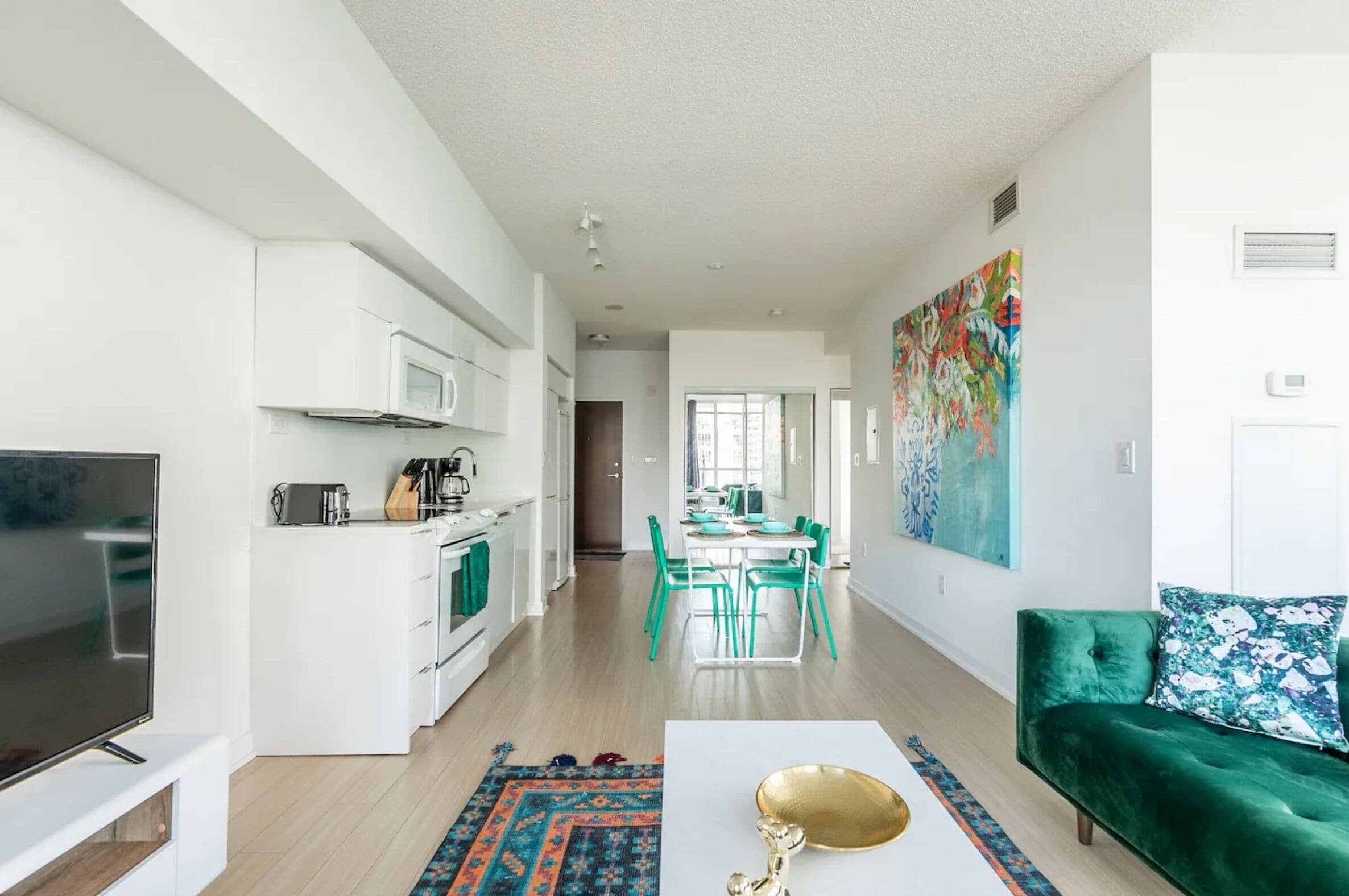 A modern living room with a flat-screen TV, a green sofa, and a dining area with a table and chairs.