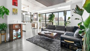 A modern living room with a grey sofa, a coffee table, and a glass cabinet. There are large windows and a view of the city. - Ohio Global Stay (Toronto)