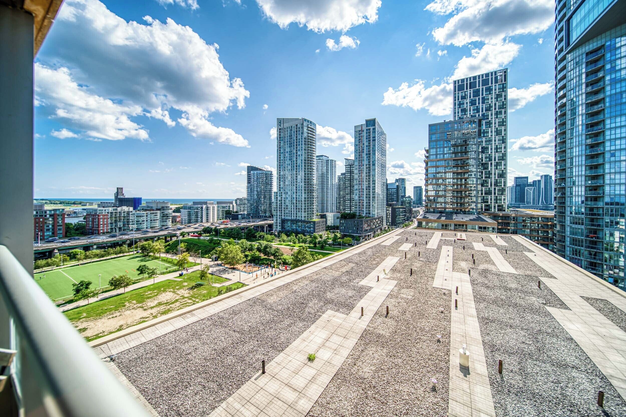A cityscape with modern high-rise buildings, a large open plaza with geometric patterns, and a distant view of a sports field.