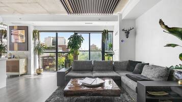 A modern living room with a sectional sofa, a coffee table, and a large window offering a city view.