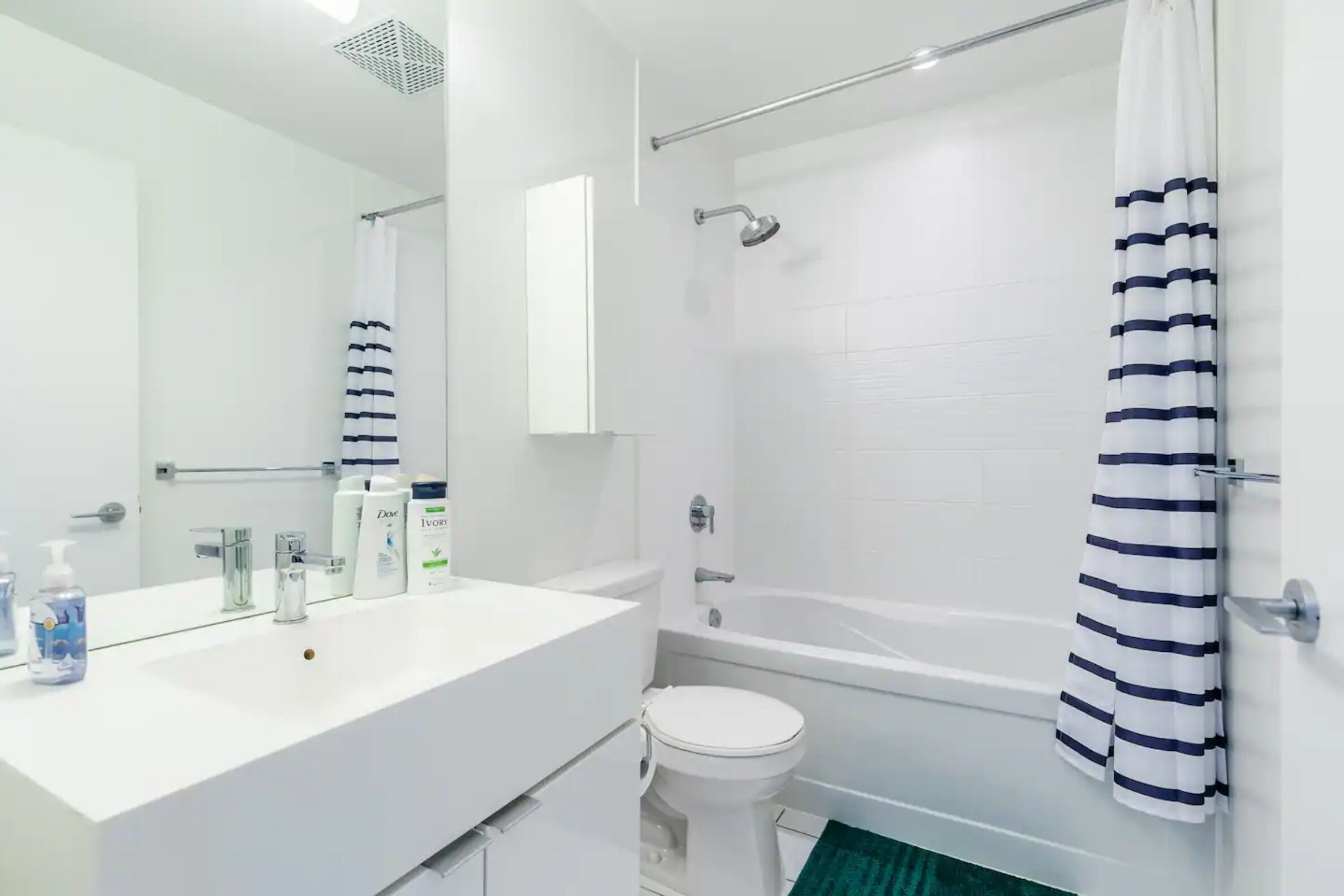 A modern bathroom with a white vanity, a toilet, a bathtub, and a shower.
