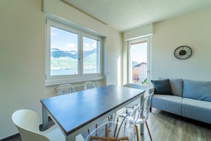 A modern living space with a dining area, a sofa, and a view of mountains. - Casa Giulia by Wonderful Italy (Lezzeno)