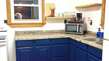 Una cocina con armarios azules, microondas, cafetera y ventana con vista a la luna.