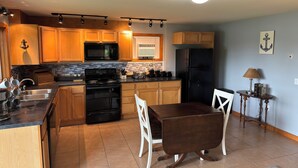 A kitchen with wooden cabinets, a black refrigerator, a stove, and a dining table with chairs.