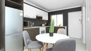 A modern kitchen with white cabinets, a stainless steel refrigerator, and a dining table with two chairs. - Madison Palms Sandton Apartment (Sandton)
