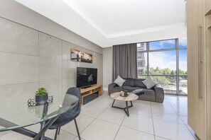 A modern living room with a sofa, TV, and a dining area with a glass table.