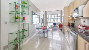 A modern kitchen with glass shelving, a dining area with clear chairs, and a view to the living room. - Hydro Park Penthouse Loft (Sandton)