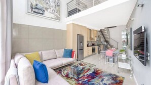 A spacious living area with a sofa, a glass coffee table, and a kitchen in the background. - Hydro Park Penthouse Loft (Sandton)