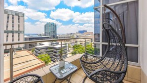 A balcony with a view of a cityscape, a hanging chair, and a small table with a plant. - Hydro Park Penthouse Loft (Sandton)