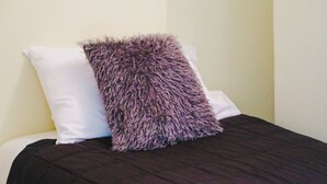 A bed with a dark-colored bedspread and a white pillow. - Single Room With Shared Bathroom (Capertee)