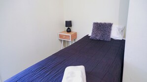 A neatly made bed with a dark blue bedspread and a folded white towel. - Single Room With Shared Bathroom (Capertee)