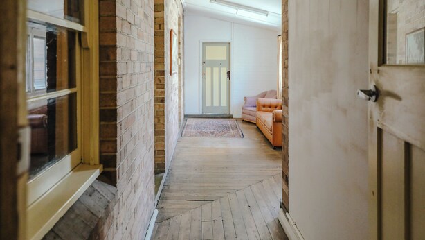 A narrow hallway with wooden flooring, a brick wall on one side, and a white door at the end. - Single Room With Shared Bathroom (Capertee)