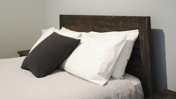 Un lit avec une tête de lit en bois, deux oreillers et un couvre-lit blanc.