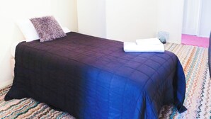 Un lit bien fait, recouvert d’une couvre-lit bleu foncé et agrémenté d’un oreiller moelleux, une serviette blanche pliée au pied du lit et un tapis à motifs.