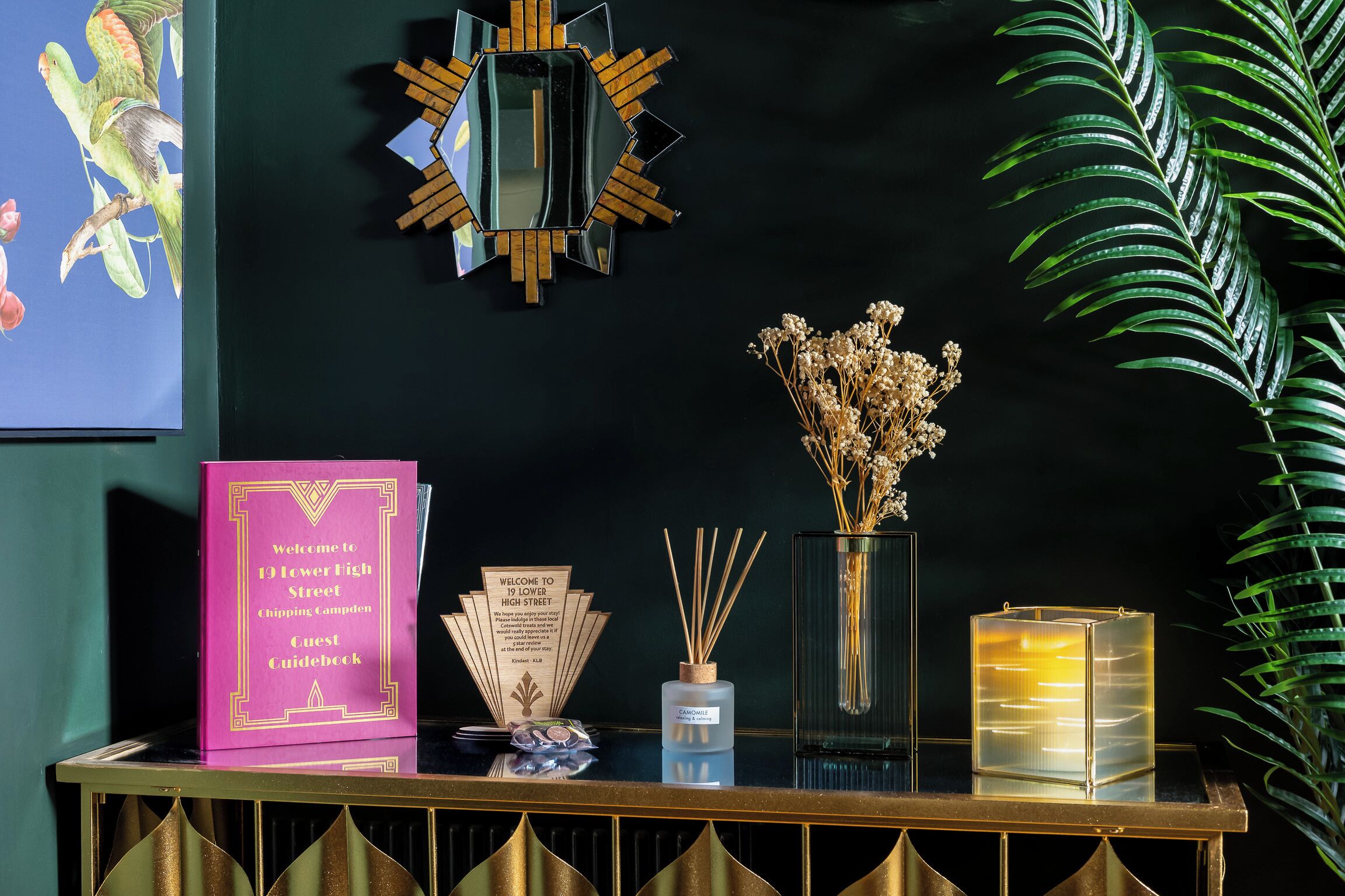 A reception desk with a guest guidebook, a mirror, a vase with dried flowers, reed diffusers, and a candle.