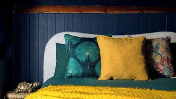 Een bed met een groene sprei, een gele deken en drie kussens met verschillende patronen.