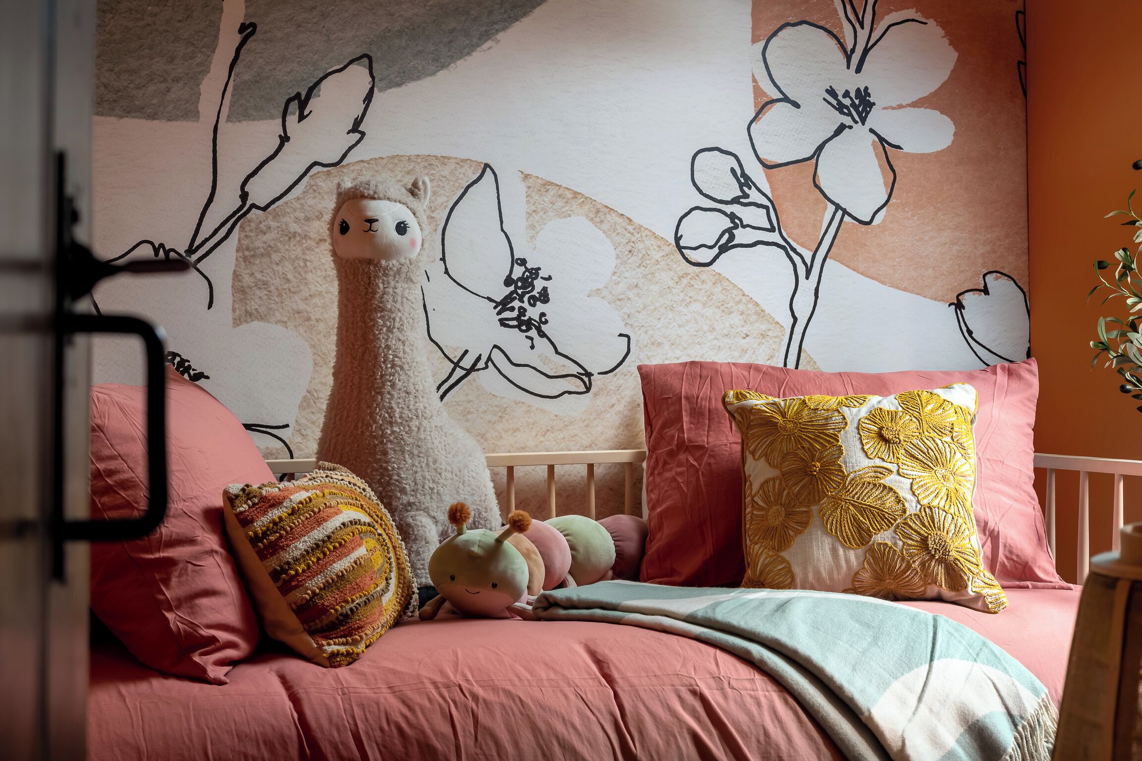 Ett mysigt sovrum med ett rosa sängöverkast, en fluffig vit kudde och en dekorativ vägg med blommönster.