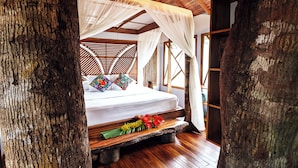 Un lit à baldaquin, un plancher en bois et un arrangement décoratif d’oreillers.