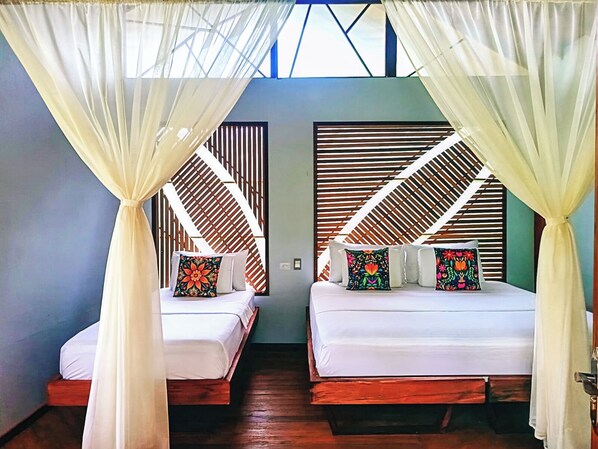 Two beds with white linens, each with a colorful pillow, under a canopy. - Buru Nature Hotel (Leticia)