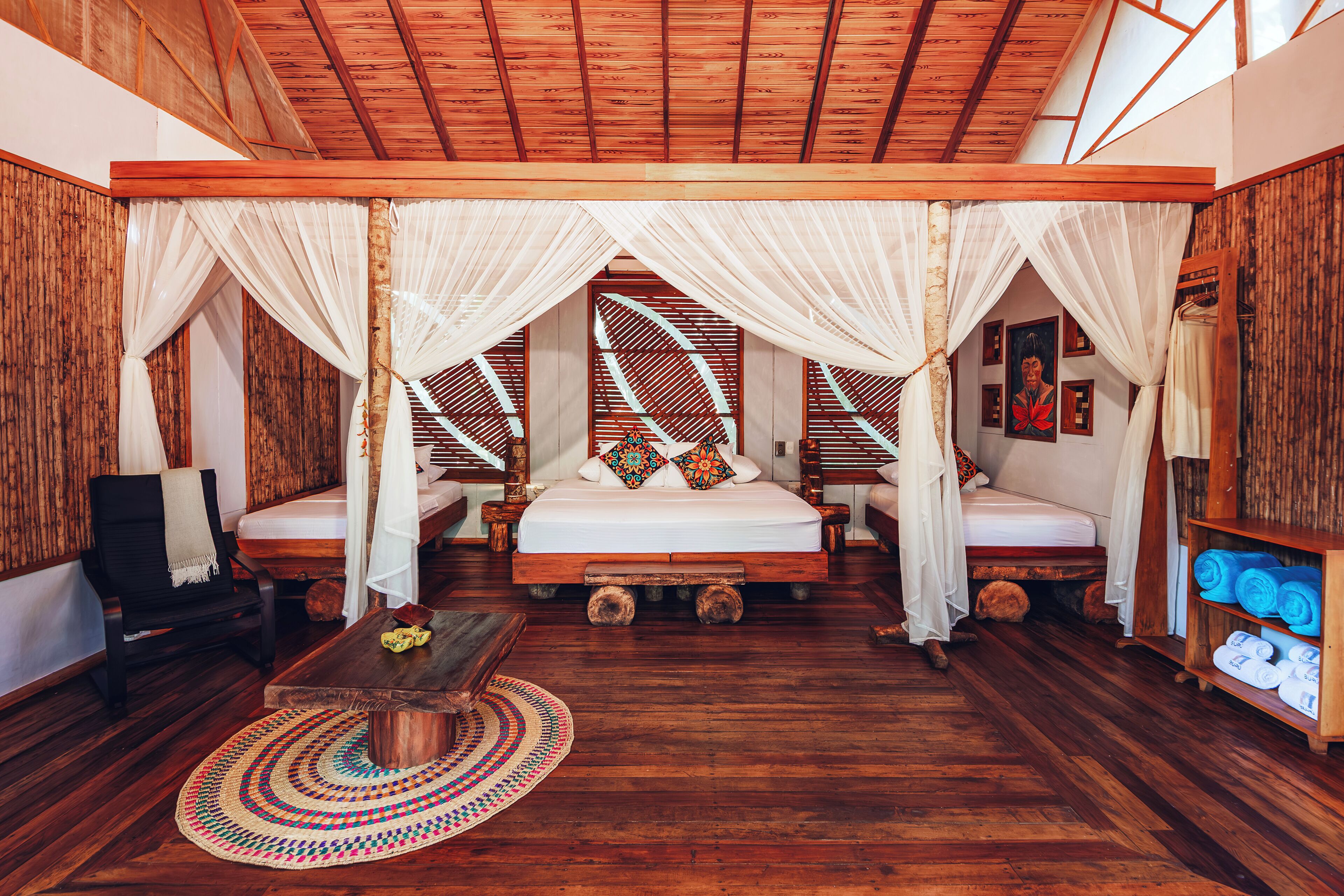 A spacious room with a large bed, two smaller beds, a wooden floor, and a ceiling with wooden beams.