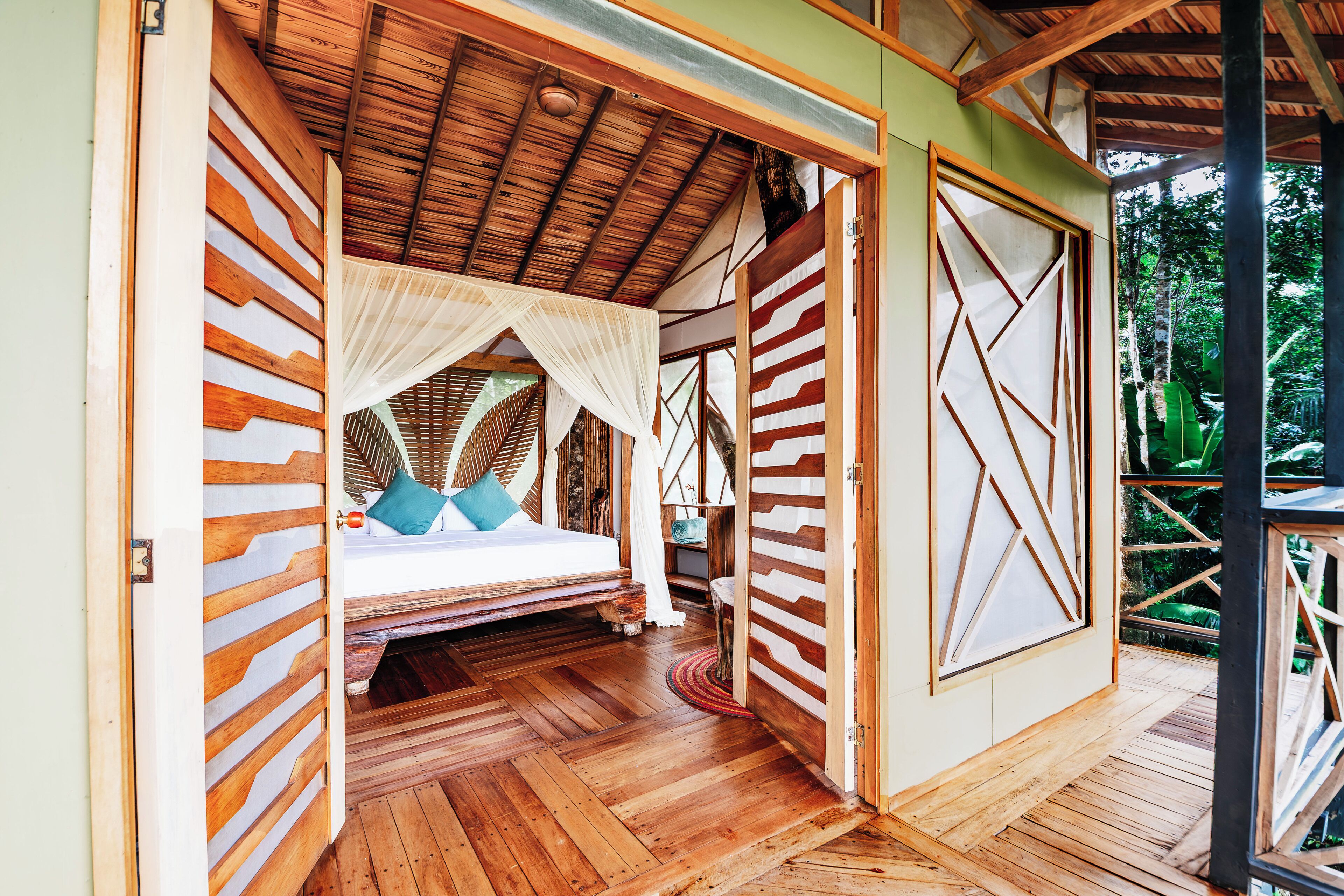 Ein Schlafzimmer mit Holzboden, einem Bett, einem Baldachin und Blick ins Freie.