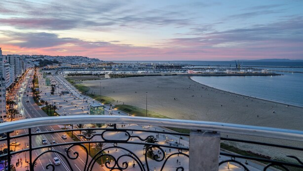 A coastal cityscape with a wide beach, a busy road, and a clear sky. - Siréna Del Tánger (Tanger)