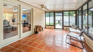 Un solarium con suelo de baldosas, ventilador de techo y vista al patio trasero.
