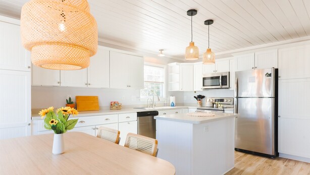 A modern kitchen with white cabinets, a central island, stainless steel appliances, and wicker pendant lights. - Walk to Beach | Luxe Home W/ Backyard, Gym, Office (Carolina Beach)