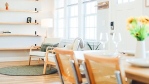 A bright living room with wooden shelves, a sofa, and a dining table with chairs. - Walk to Beach | Luxe Home W/ Backyard, Gym, Office (Carolina Beach)