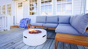 A deck with a round fire pit, a blue sofa, and a wooden bench. - Walk to Beach | Luxe Home W/ Backyard, Gym, Office (Carolina Beach)