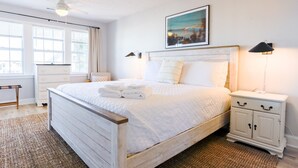 A neatly made bed with folded towels, a bedside table with a lamp, and a window with blinds. - Walk to Beach | Luxe Home W/ Backyard, Gym, Office (Carolina Beach)