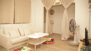 A room with a white sofa, a small white table, a fan, and a colorful bean bag. - Friend's House Arak  (Chiang Mai)