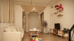 A living room with a sofa, a small table, a fan, a TV, and a colorful cushion. - Friend's House Arak  (Chiang Mai)