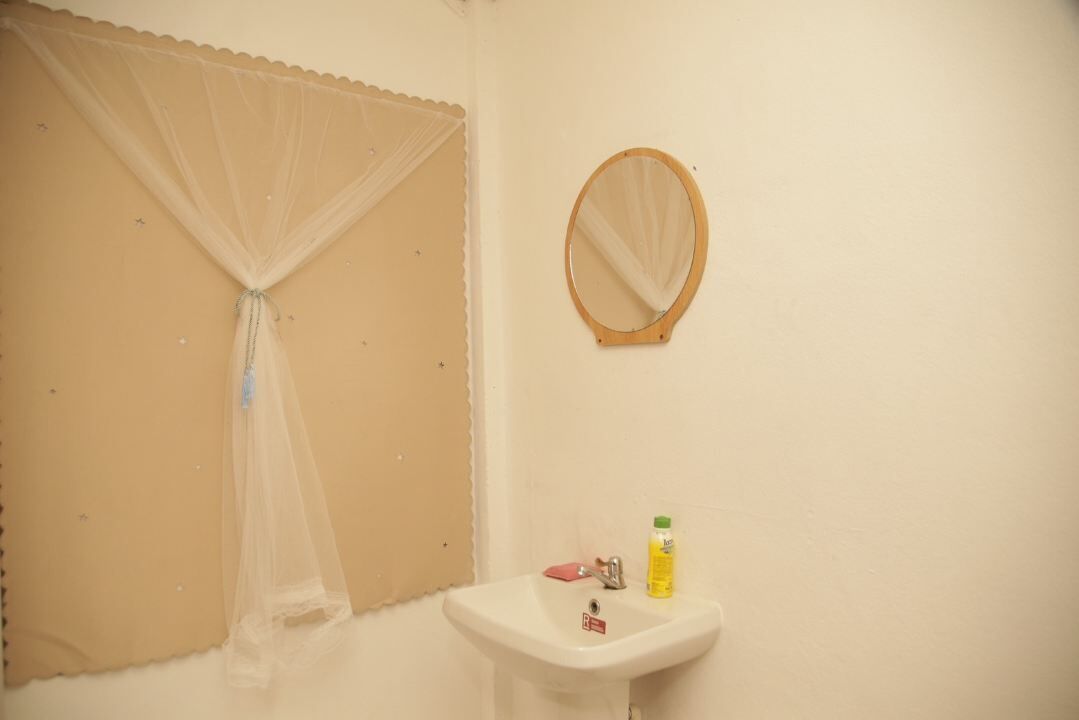 A bathroom with a sink, a mirror, and a window with a sheer curtain.