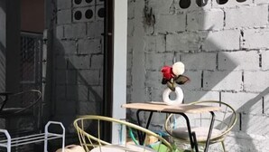 A small outdoor seating area with two chairs and a table, a white brick wall with circular cutouts, and a green artificial turf floor. - Friend's House Arak  (Chiang Mai)