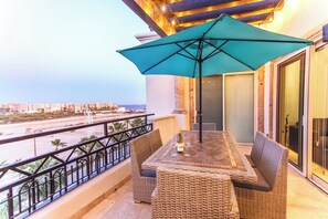 A balcony with wicker furniture, a table, and a large umbrella.