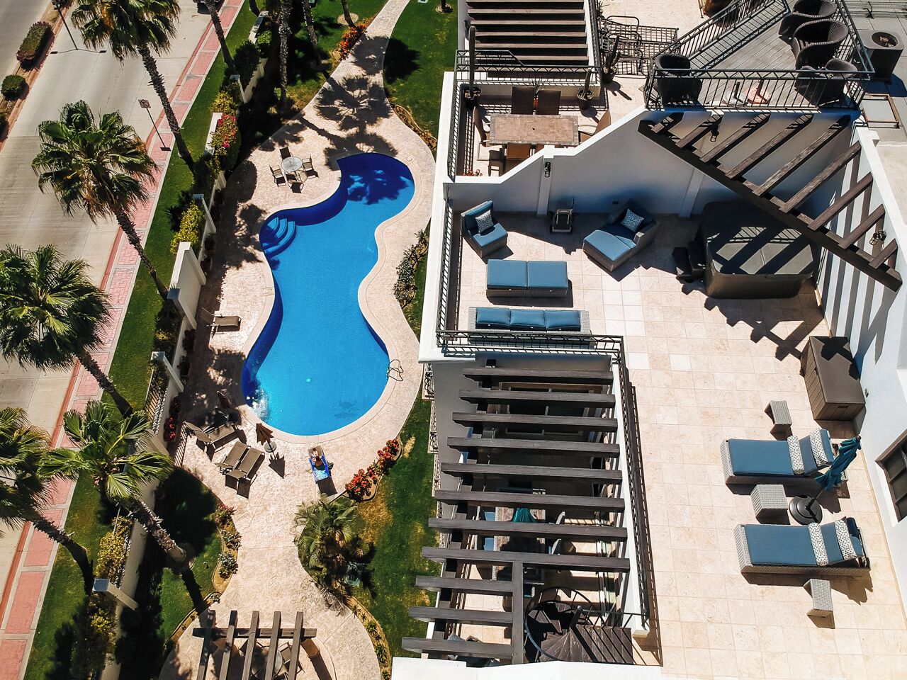 An aerial view of a hotel with a swimming pool, outdoor seating, and a staircase. - CABO PENTHOUSE CONDO - Rooftop deck with Private Jacuzzi at Puerta Cabos Village (Cabo San Lucas)