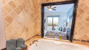 A bathroom with a large bathtub, a wicker basket with towels, and a view of a bedroom with a bed and a balcony. - CABO PENTHOUSE CONDO - Rooftop deck with Private Jacuzzi at Puerta Cabos Village (Cabo San Lucas)