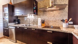 A modern kitchen with dark cabinets, granite countertops, stainless steel appliances, and a granite backsplash. - CABO PENTHOUSE CONDO - Rooftop deck with Private Jacuzzi at Puerta Cabos Village (Cabo San Lucas)