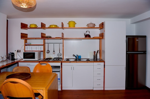 A compact kitchen with white cabinets, a microwave, a stove, and a refrigerator. There are wooden shelves above the stove holding pots and pans. - Casa Claudia by Wonderful Italy (Bellagio)